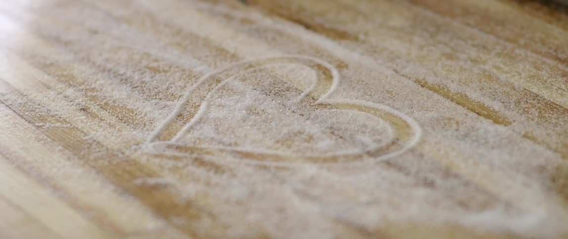 A heart has been drawn in sugar spilt on a wood surface