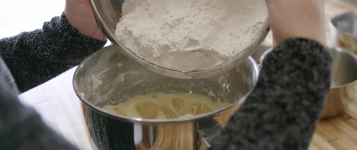 Flour is being poured into a bowl of batter