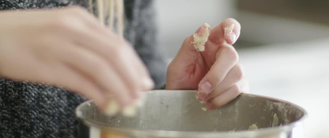 A woman picks dough out of a mixing bowl