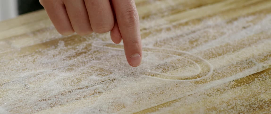 A person draws a heart in sugar on a cutting board
