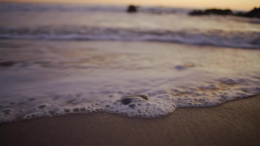 The ocean tide washes over a stone on a beach at sunset