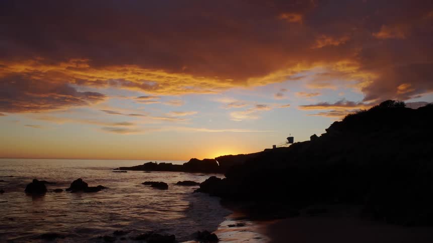 Waves rolling in to the shore as a bird flies overhead as the sun sets