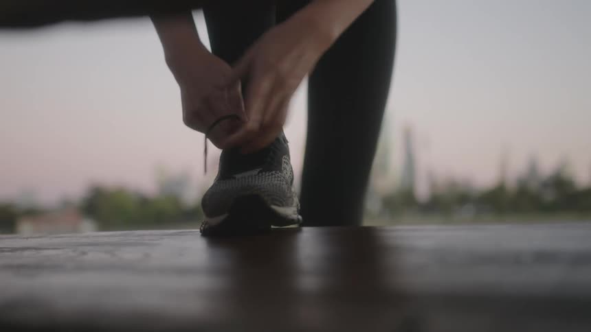 Woman with her running shoes on top of a bench tying her shoelaces
