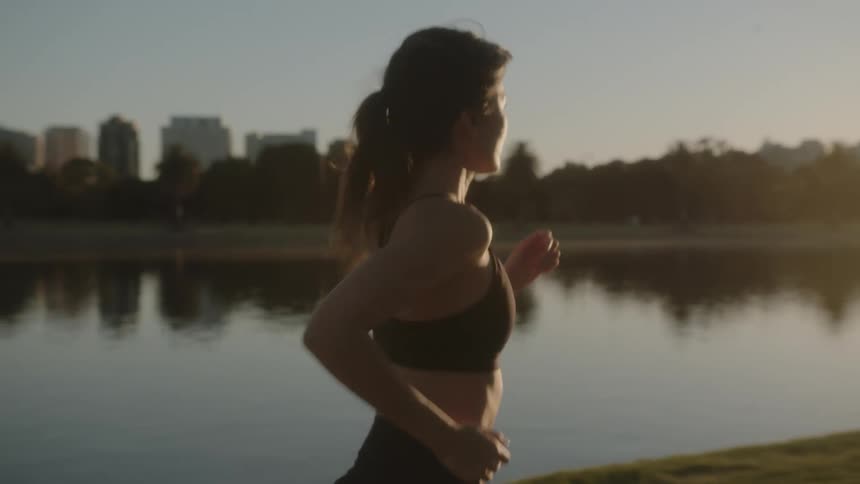 Young woman jogging alongside lake shoreline in the city