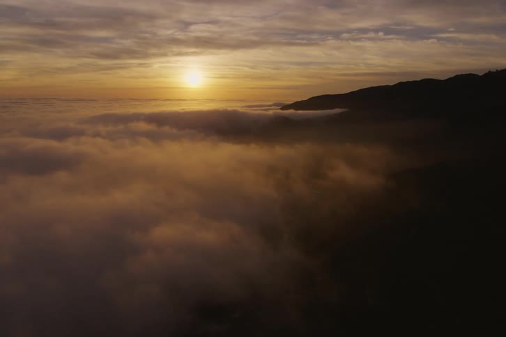 The sun is shining brightly above the clouds with a mountain on the horizon