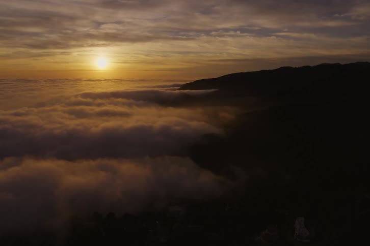 Sunlight reflects on the clouds high in the sky near a mountain
