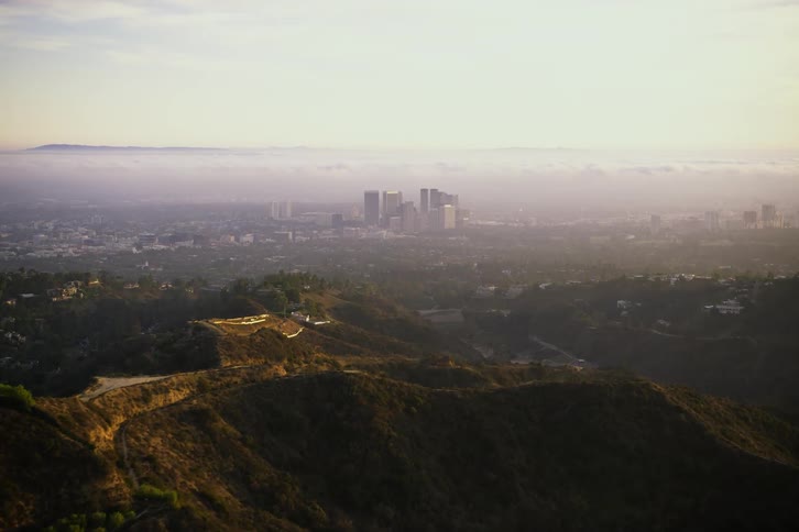 Skyscrapers shrouded in fog loom in the distance from a hilly countryside