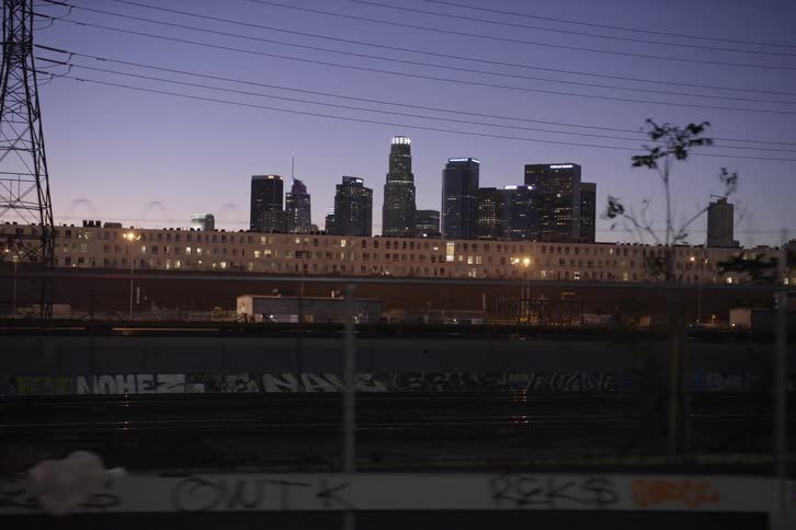 Power lines and train tracks pass shipping center with city skyline as a backdrop