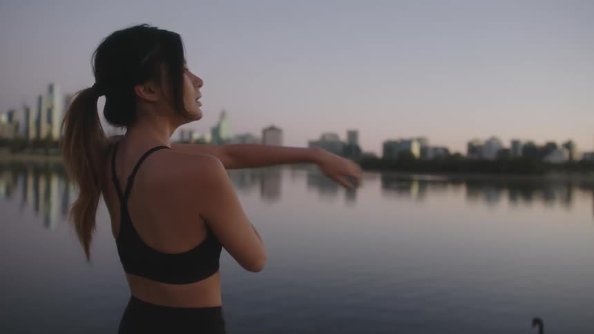 A woman is stretching by a lake at dusk