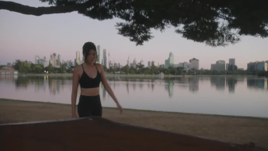 A woman stops to tie her shoes by the water