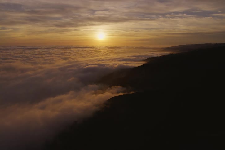 An aerial view of the sun over clouds by a hillside
