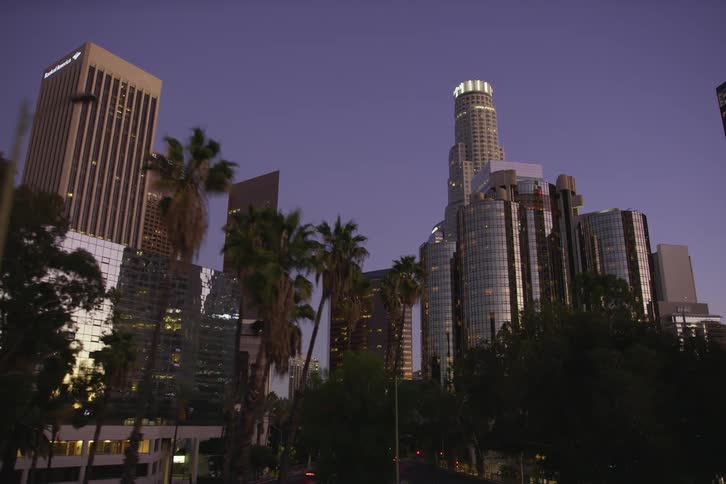 City skyscrapers and high rise buildings seen from moving car on highway at dusk