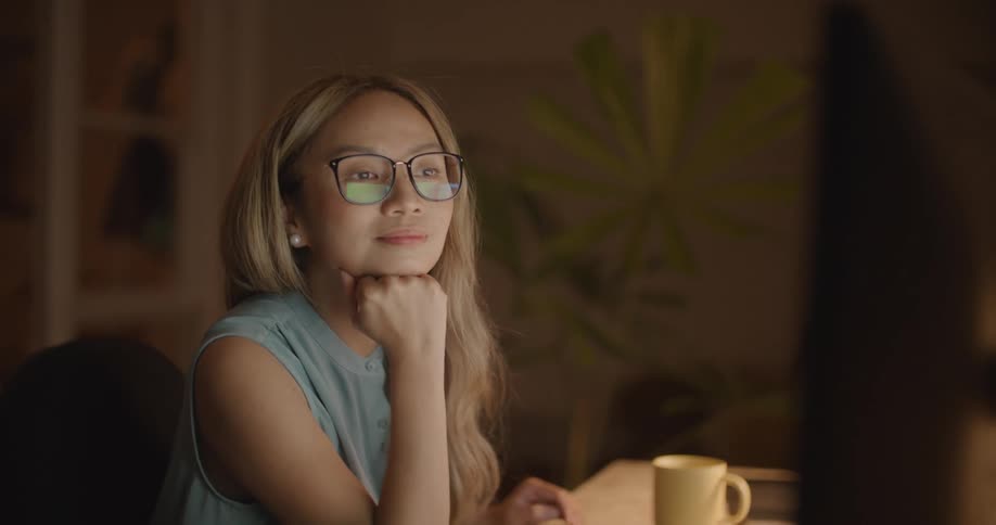 A young woman sits at home and smiles as she video chats on her computer