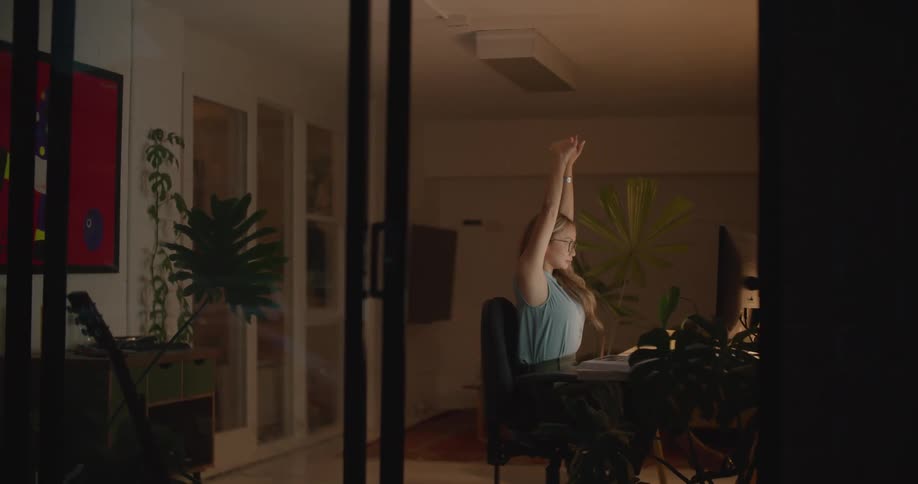A woman is stretching at her desk inside