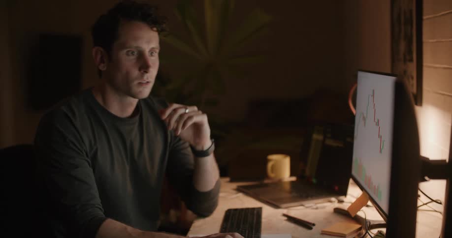 Man in gray sweatshirt works on computer in room at night