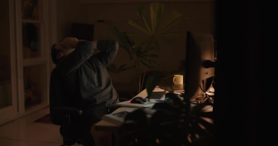 Frustrated man sitting at desk working on computer late at night
