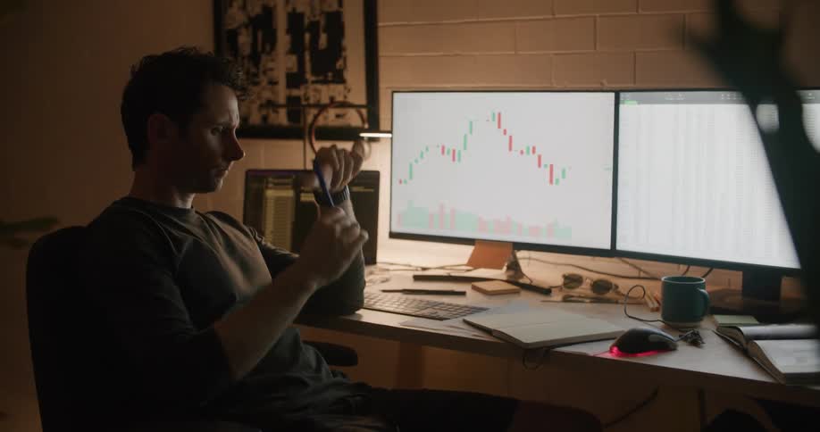 A man yawns and scratches his eyes as he sits at his desk at night