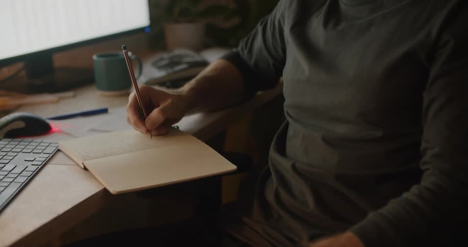 A man writes in his notebook at his desk