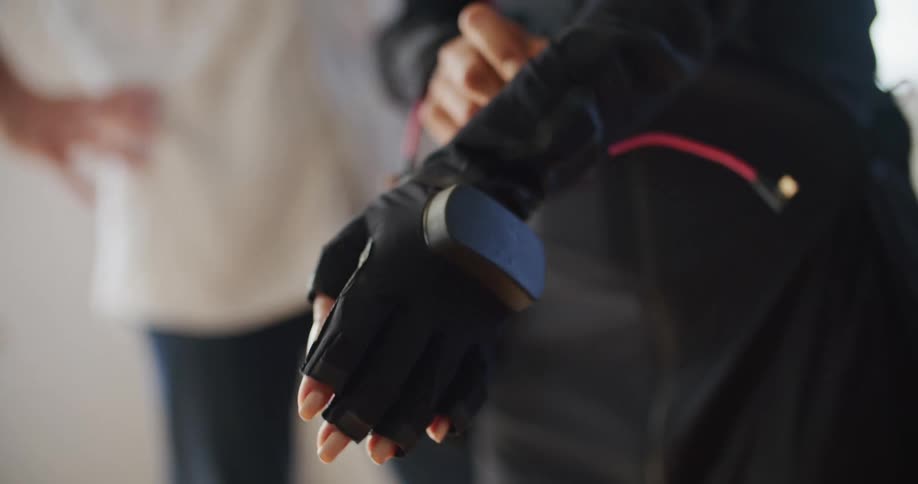 Long black glove with no finger tips and with a wire connected to it is being pulled on to a hand