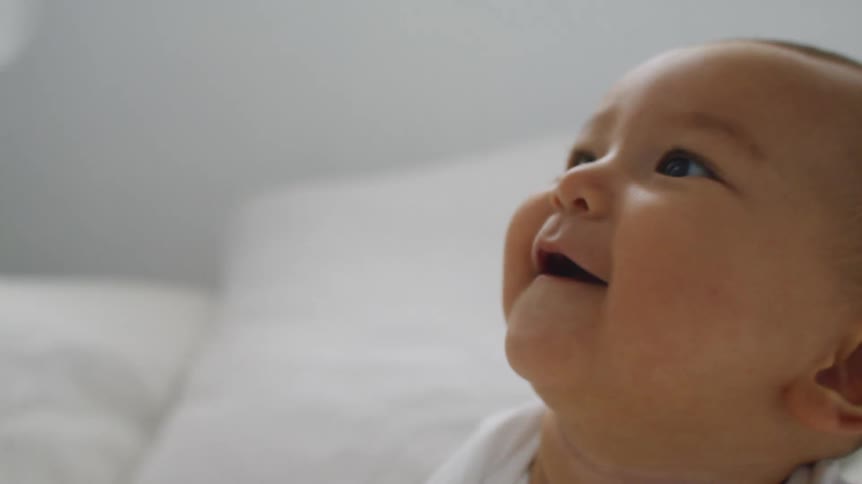 A baby is smiling as a cloth is waved in his face