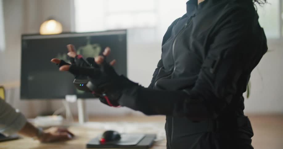 A woman wearing a motion capture suit moves her hands and the movement is shown on a monitor