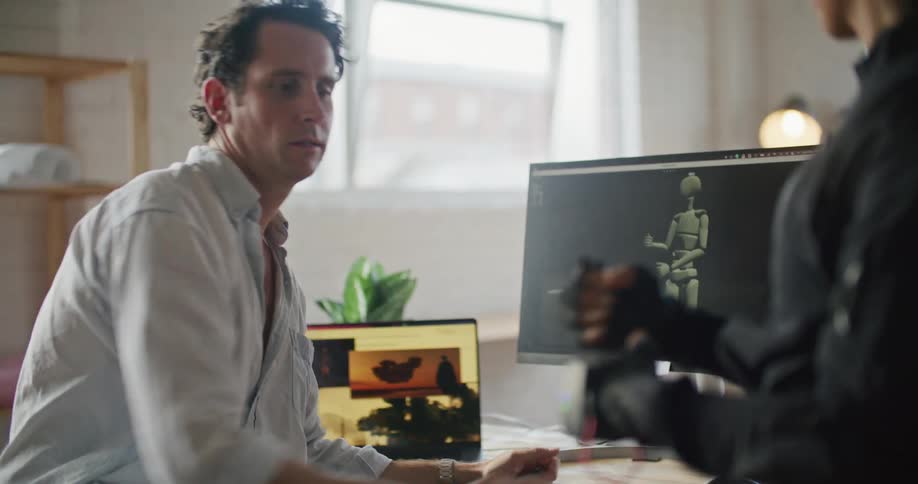 Man sitting near computer screen with animated mannequin guides woman wearing motion capture suit through gestures wanted
