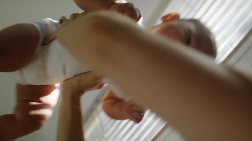 A woman at home plays with her baby and holds him above her head
