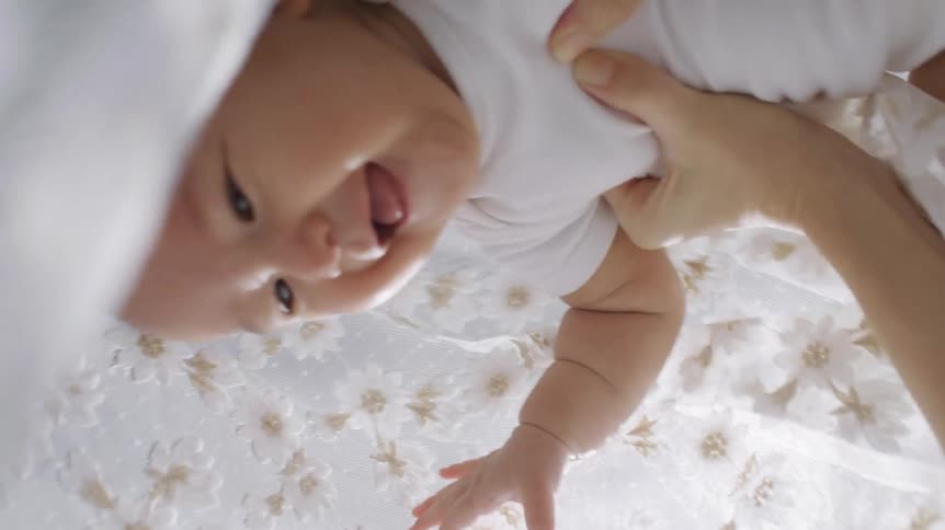 A person lifts a baby up who then laughs