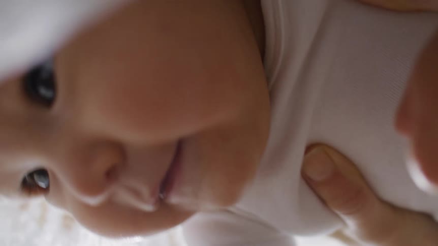 A persons hand holding a baby up inside a blanket while the baby smiles and laugh