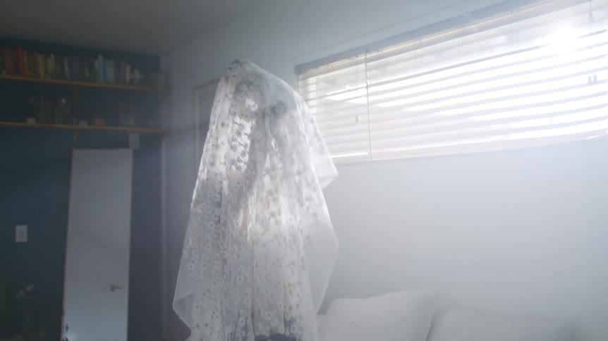 A woman holds her baby in the air with a white lace cloth draped over them