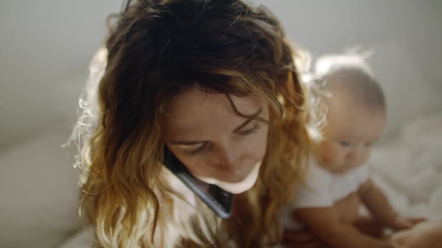 A woman is talking on the phone while holding her baby