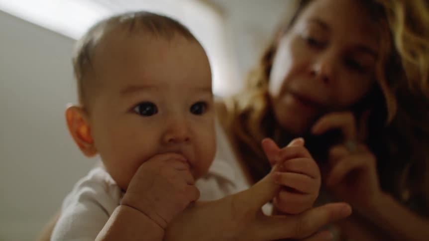 A woman at home holds her baby as she talks on a phone