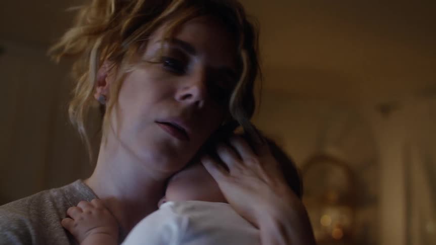 A woman at home rocks her sleeping baby as she holds him