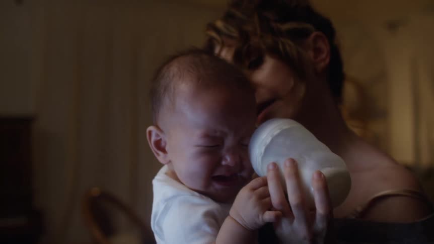 A baby cries as his mother tries to give him a bottle at home