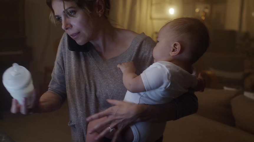 Mom holds the phone with her shoulder while trying to give baby a bottle