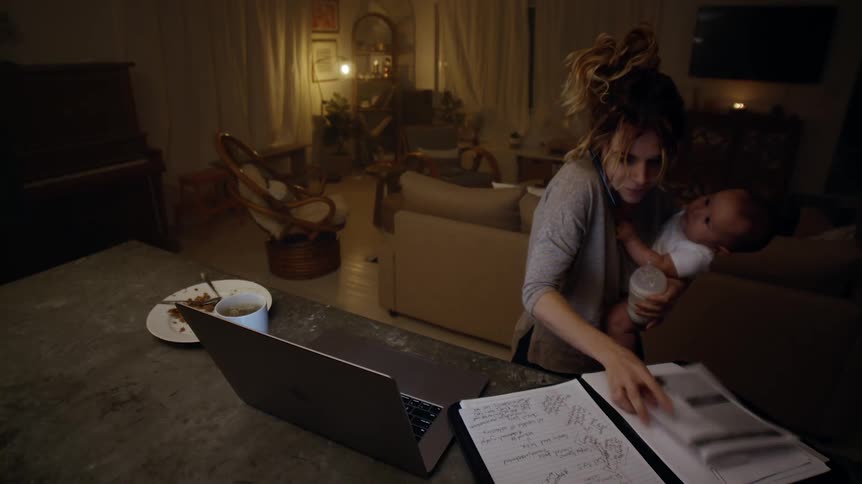 Mother working from home talks on the phone while trying to feed her baby a bottle