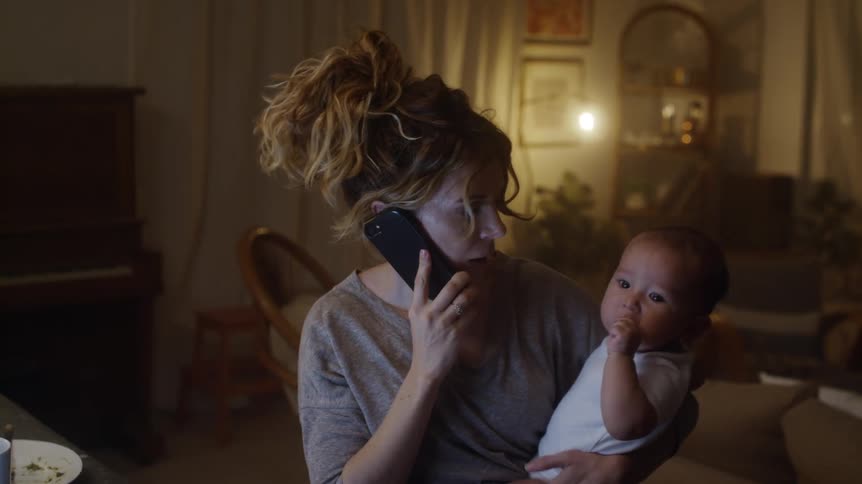 Overwhelmed mother holding baby while talking on a cell phone