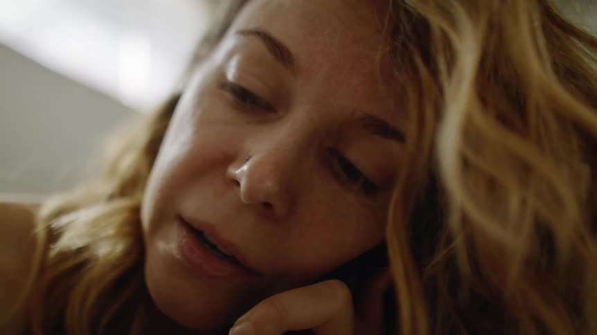 Mother with brown wavy hair holds baby and talks on smartphone