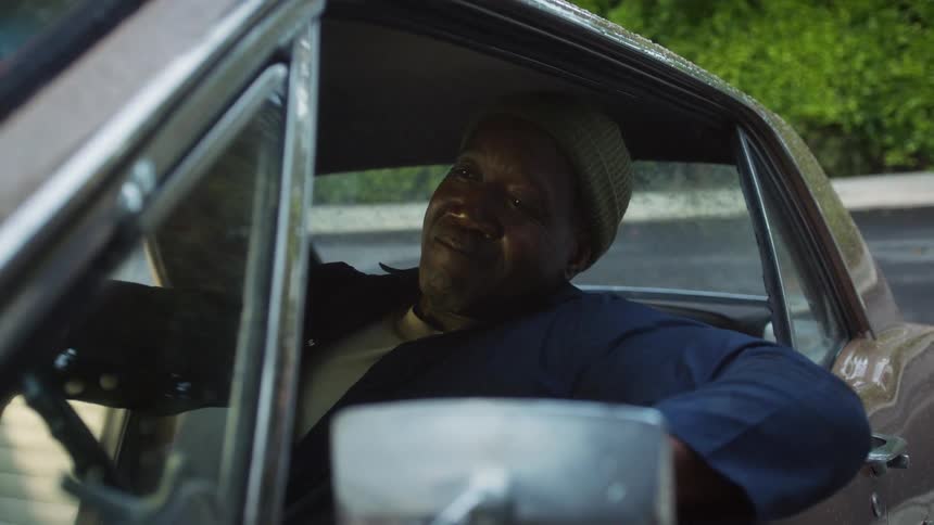 A man driving in a car pulls up and stops and leans out the window