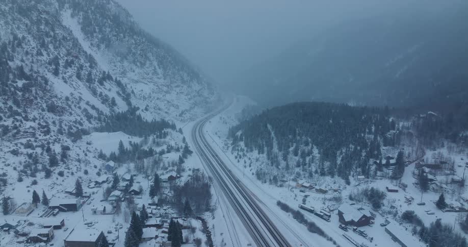 Vehicles travel on the highway next to the snowy land and mountains
