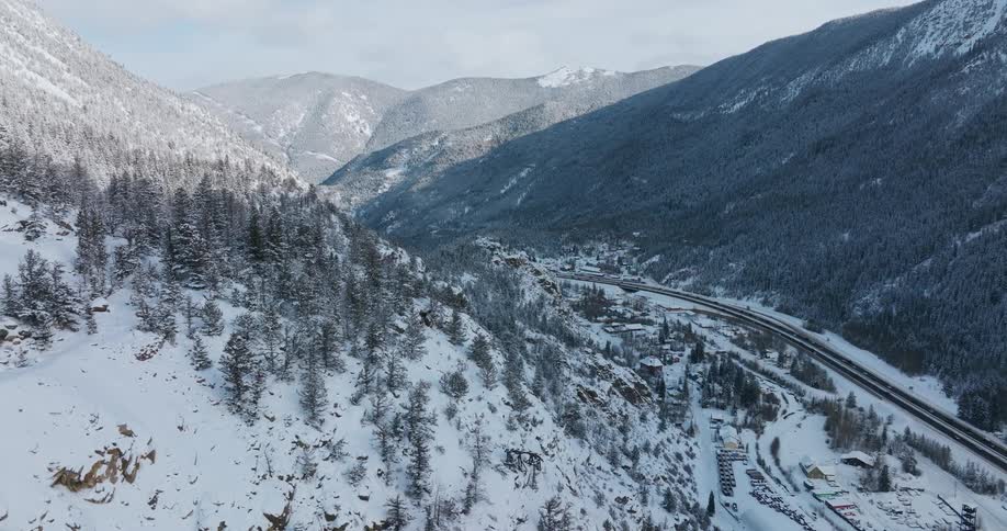 Traffic moves on a road running through a snow covered forested mountain valley on a winter day