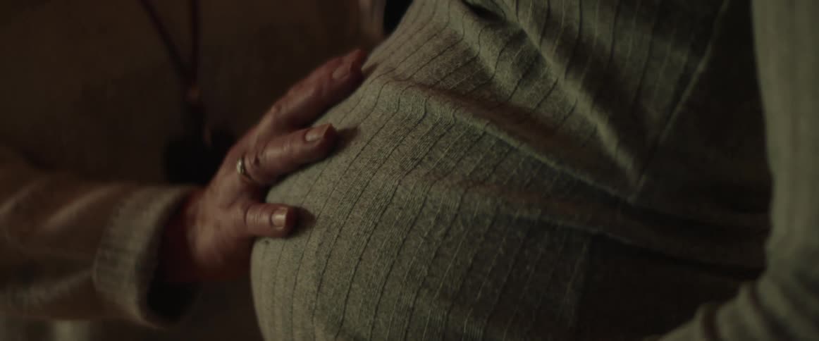 Middle aged woman with sweater touches pregnant womans belly