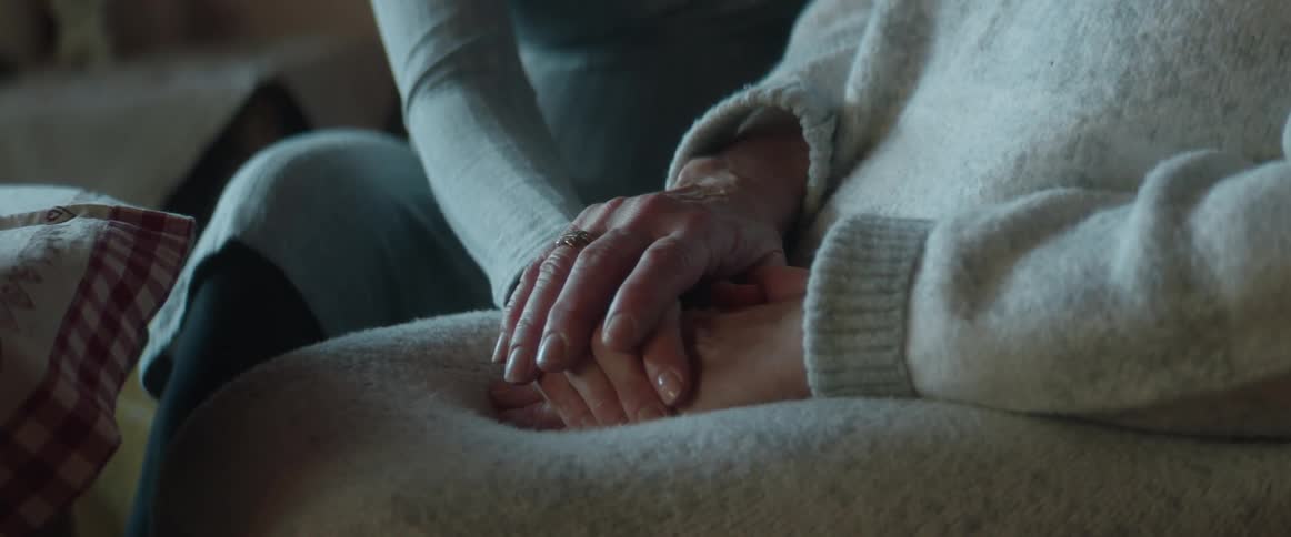 Woman sitting on the couch gently touching the hand of another older woman in a generous way