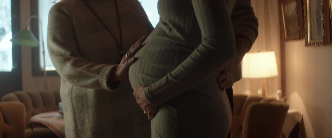 Close up of elderly woman rubbing young womans pregnant belly in living room