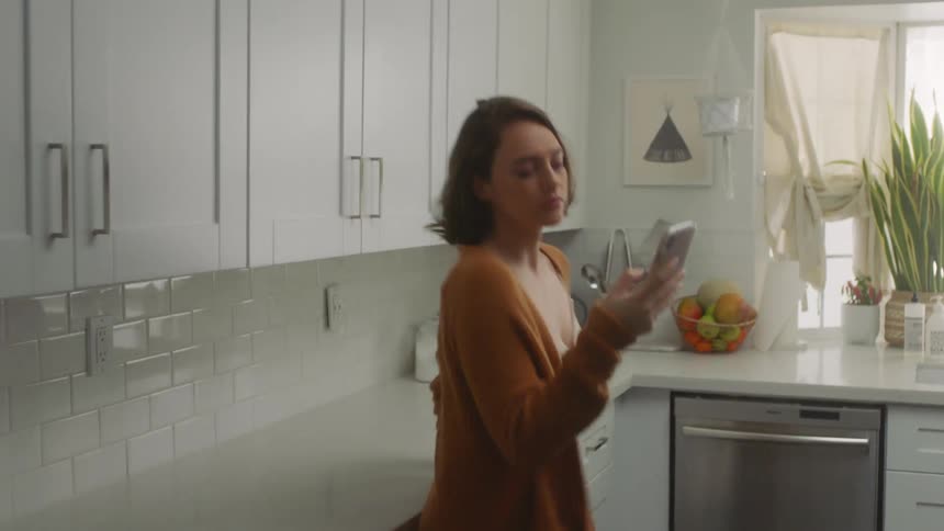 A woman is texting on her phone and walking in the kitchen