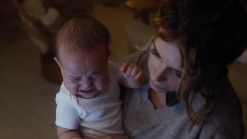 Worried mother holding her baby and checking his temperature while calling someone on the phone