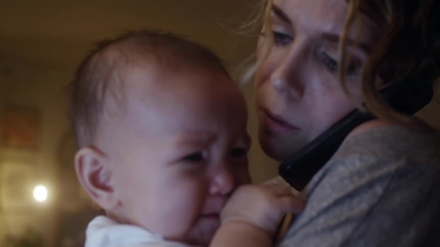 Worried mother holding and rocking her crying baby while she is talking to the phone