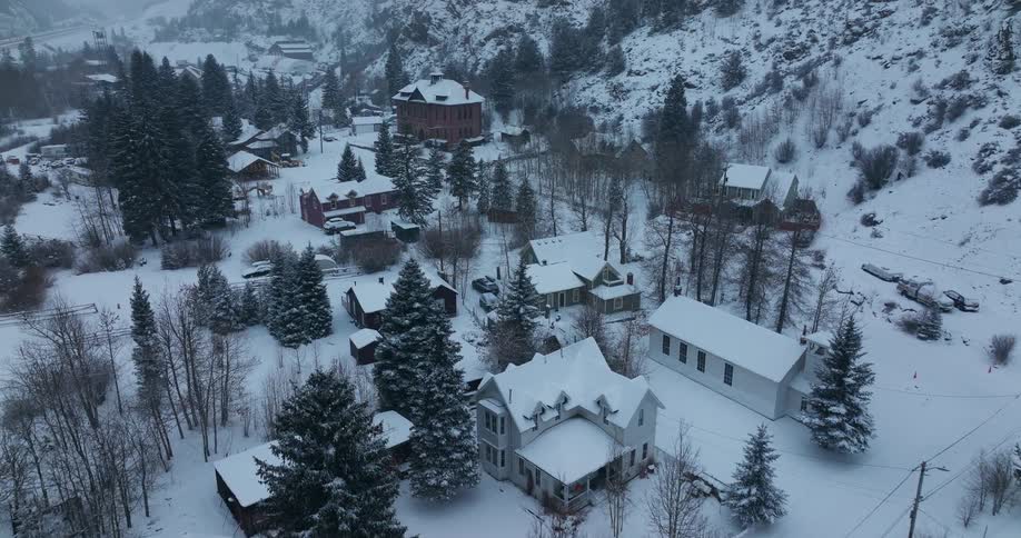 Aerial view of a snow covered mountain valley neighborhood with many tall pine trees