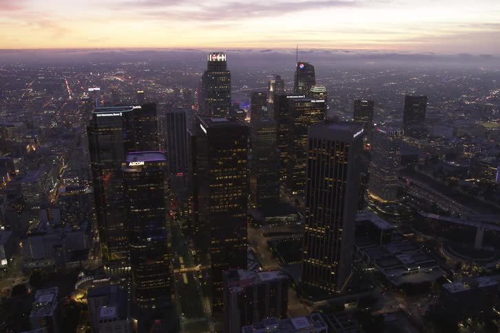 Traffic flows through downtown at night as city stretches to fog covered horizon under a red sky
