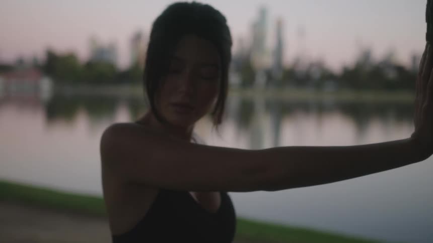Young woman in a public park leaning against a tree and stretching herself